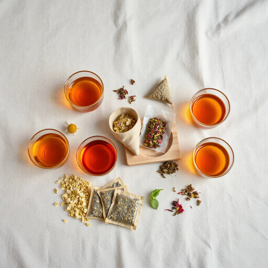 Assorted glass cups of herbal infusions with scattered dried herbs on a wooden tray