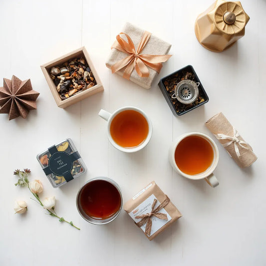 Assorted tea gift sets with tins and a warm cup of amber tea on a simple tabletop